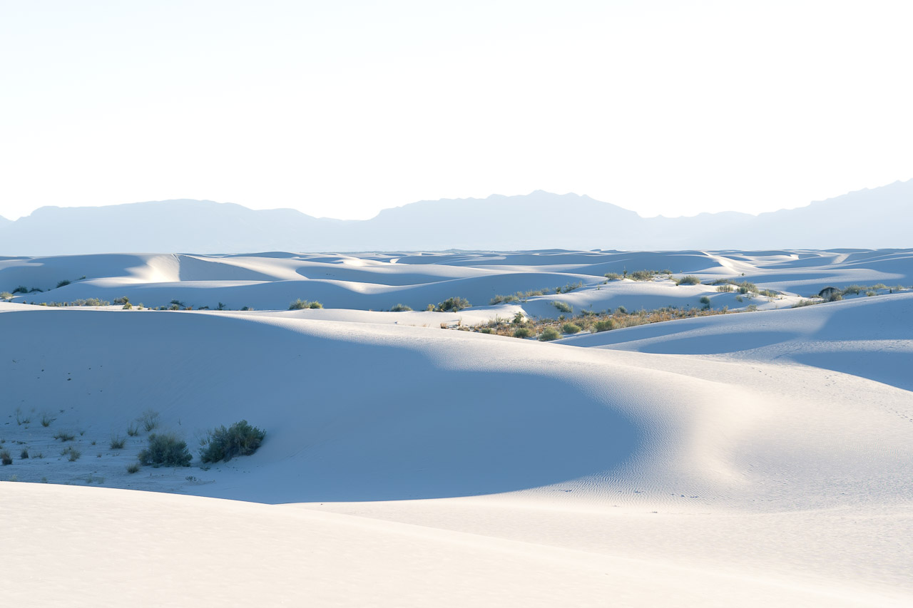 White sand dunes and distant mountains at sunset