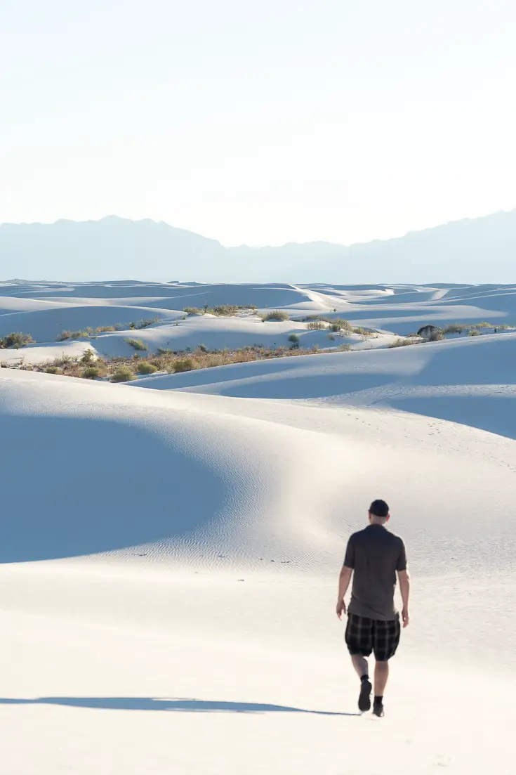 Man walking along undulating white sand dunes casting blue shadows in the golden hour light