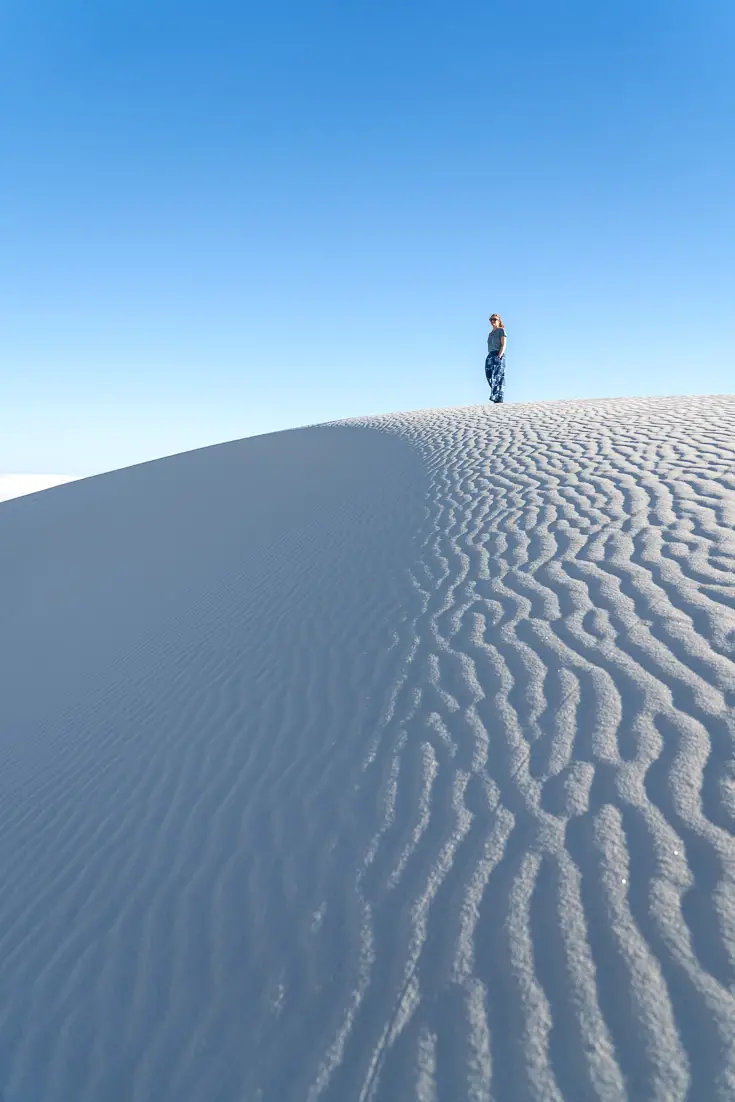 Woman standing on rippled, white, sand dune with clear, blue sky overhead