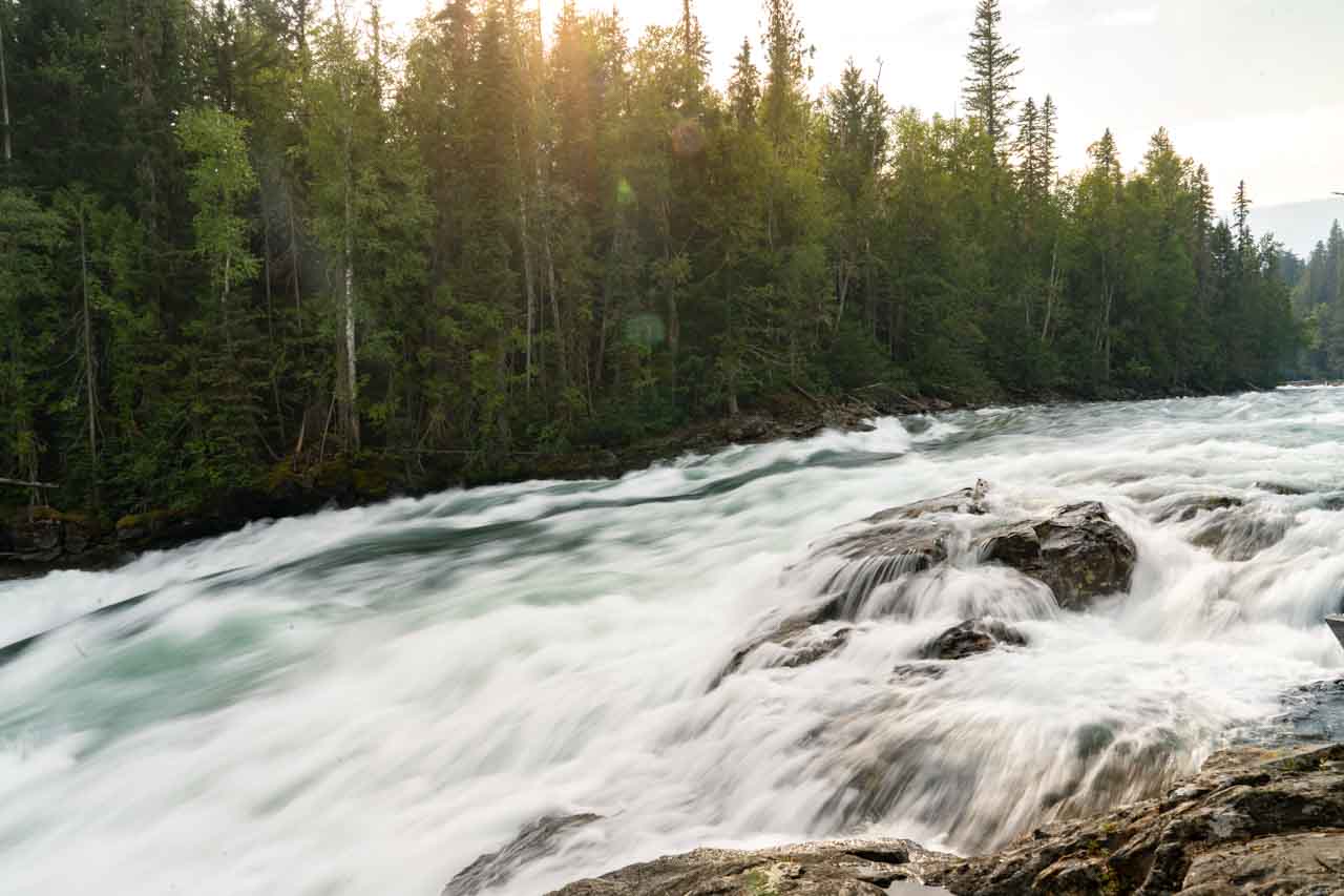 Photo of fast-moving water passing over large rocks with forest on the shore at Bailey's Chute