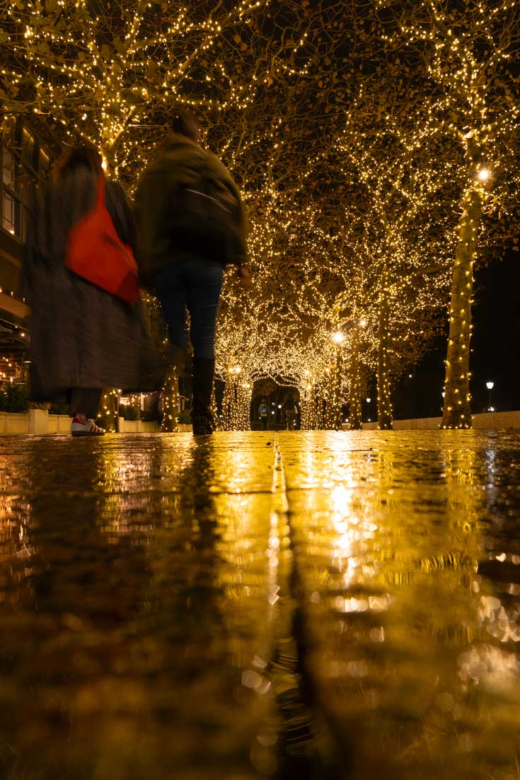 Pedestrians walking through archway created by fairy lights in trees outside Brookfield Place