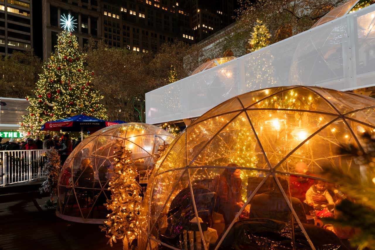 Families gathered in igloos in Bryant Park, with large Christmas tree in the background