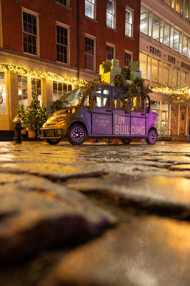 Vintage car piled with presents on cobblestone street reflecting yellow holiday lights