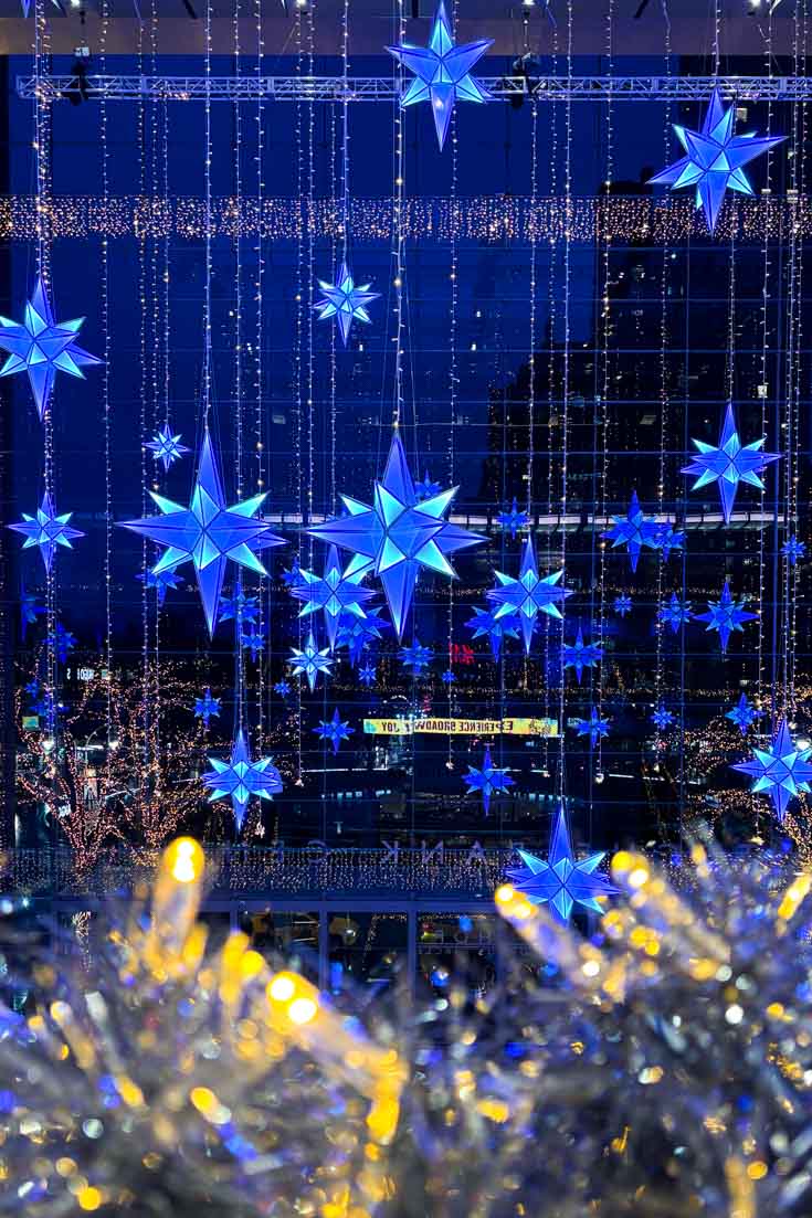 Holiday star decorations illuminated in hues of blue, hanging infront of a glass curtain wall