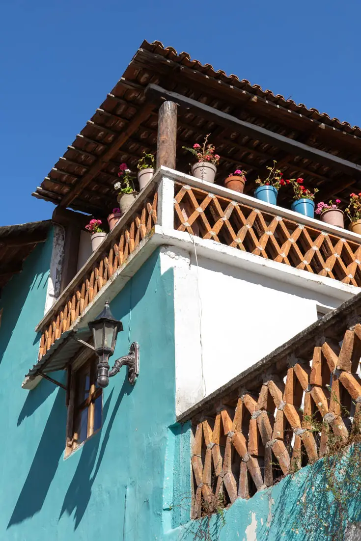 Looking up at a teal home with colourful pots of geraniums on the balcony