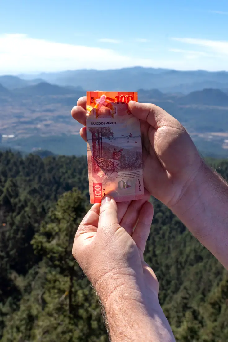 Hands holding up 100-peso bank note infront of valley and mountain view