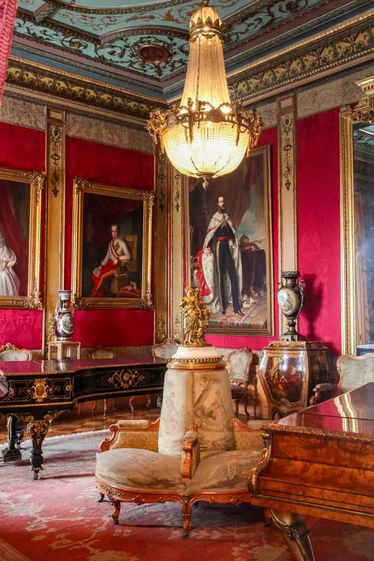 A red salon with historic portraits on the wall and a gold chandelier