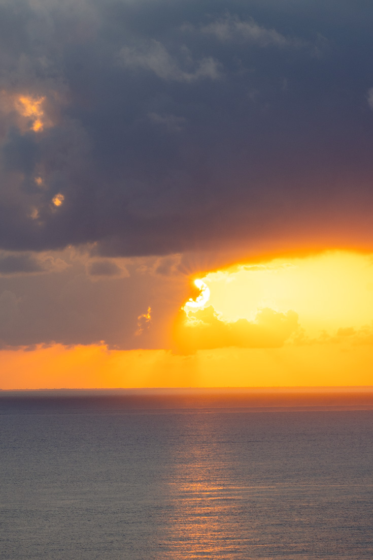 Golden sun peeking out from a blue-grey cloud at sunset