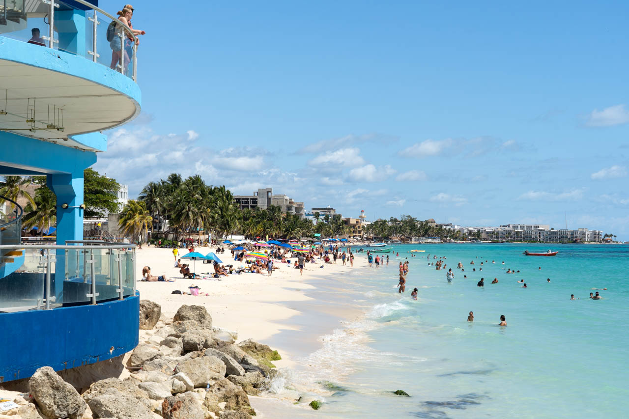 Busy, white-sand beach with blue-green water on a sunny day