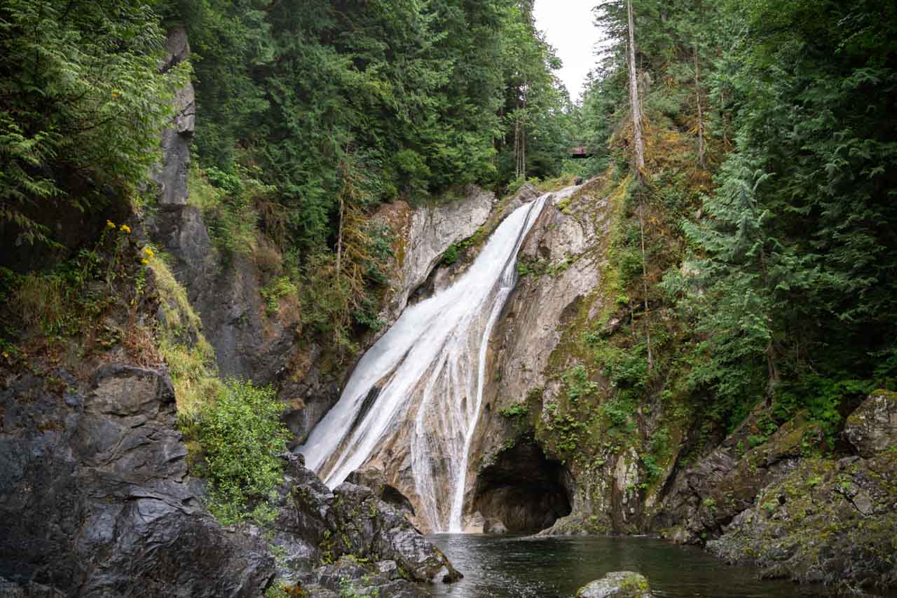 Waterfall flowing diagonally down rockface and surrounded by evergreen forest