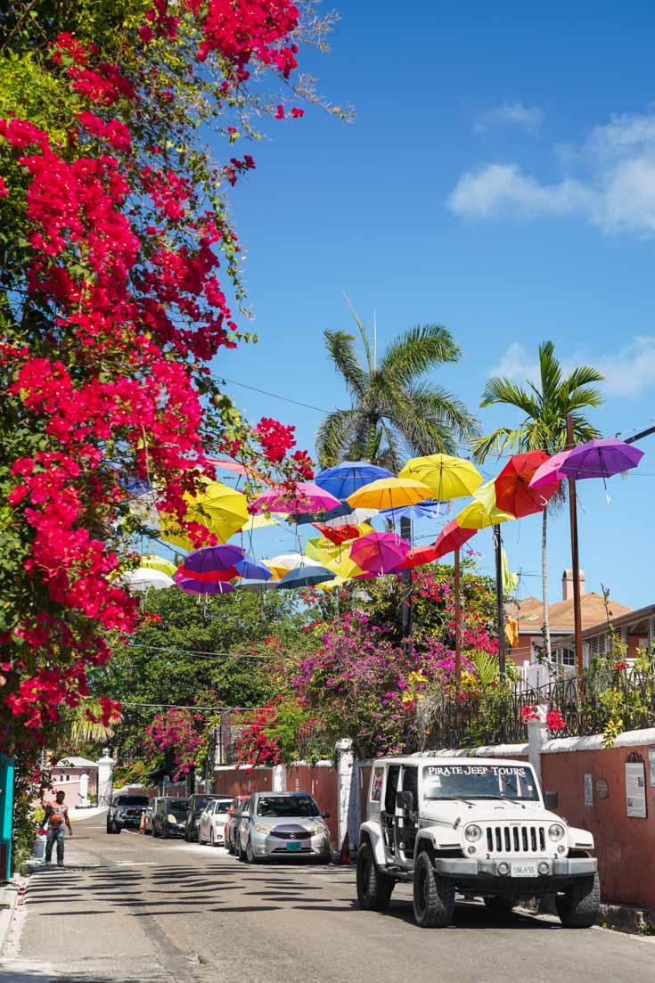 Streetscape framed by bright bouganvilleas and colourful umbrellas hanging overhead