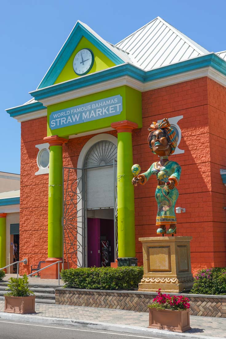 Large orange, lime and aquamarine building with column-framed entrance and a clock face above the door