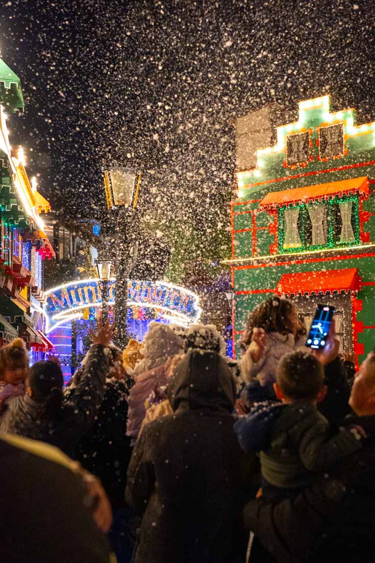 People watching Christmas lighting show in Bavarian-themed village with fake snow in the air