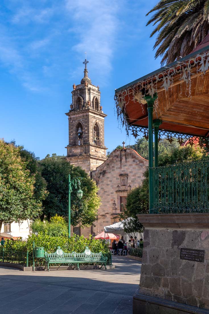 Image of church belltower across garden with bandstand and green benches