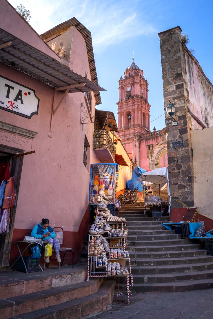 Pink church bell tower viewed above narrow staircase lined with market stalls selling decorative ceramics