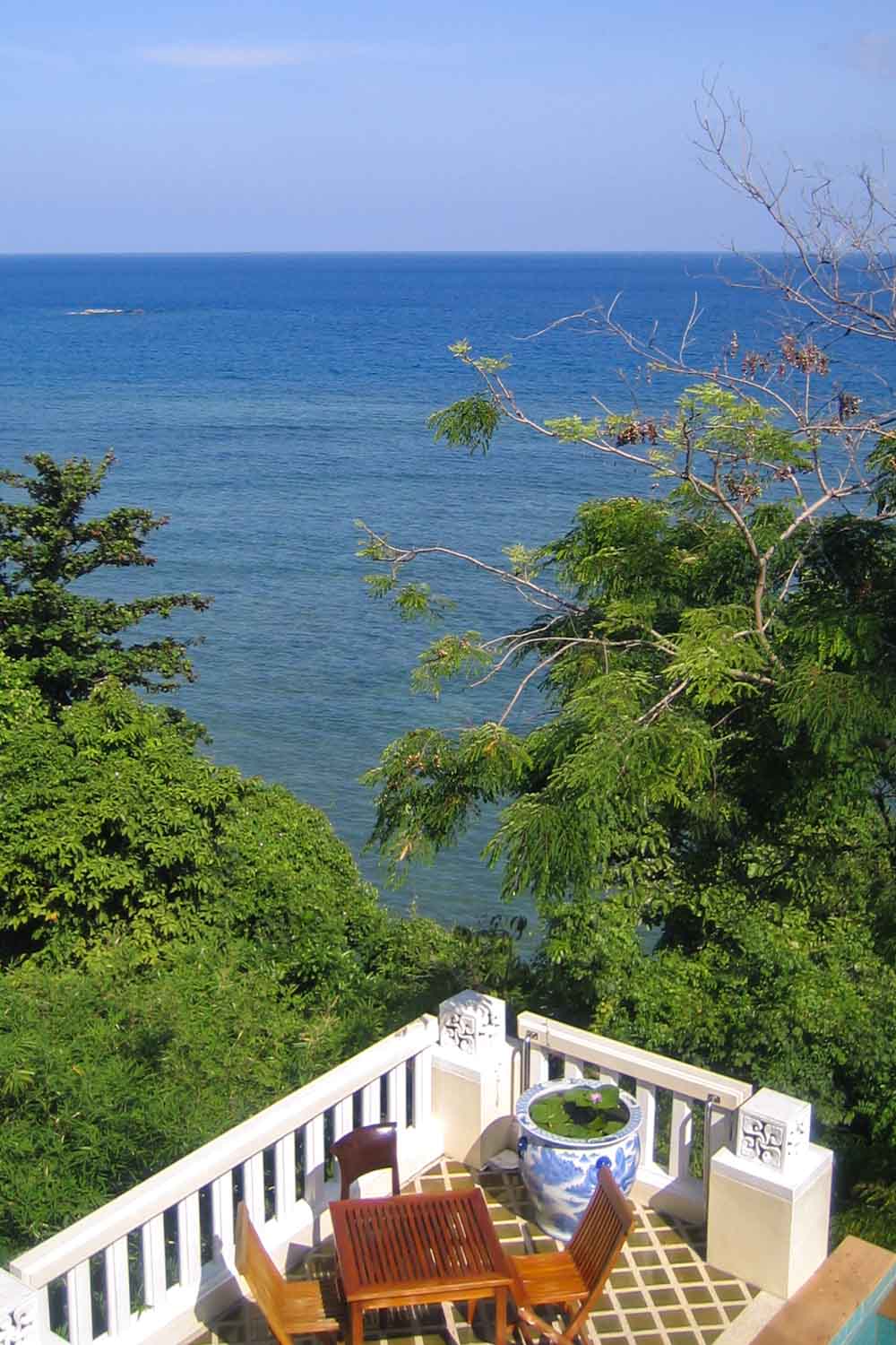 View of sea from clifftop resort in Kamala, Phuket, with tiled terrace in foreground with wooden furniture and ornamental pot