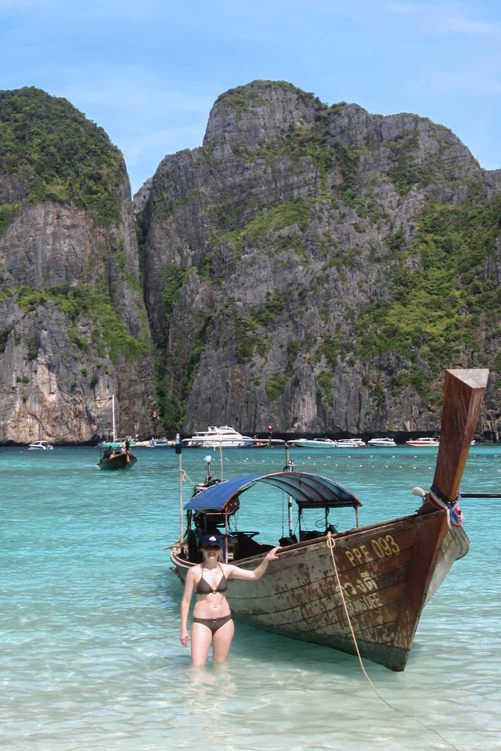 Woman standing in knee-deep tropical water, next to traditional Thai boat with limestone cliffs in the background