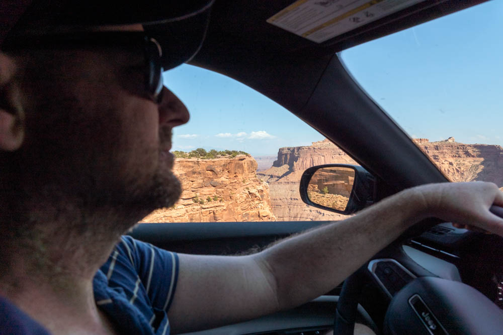 Man driving car, with view of red rock landscapes through side window and in rearview mirror