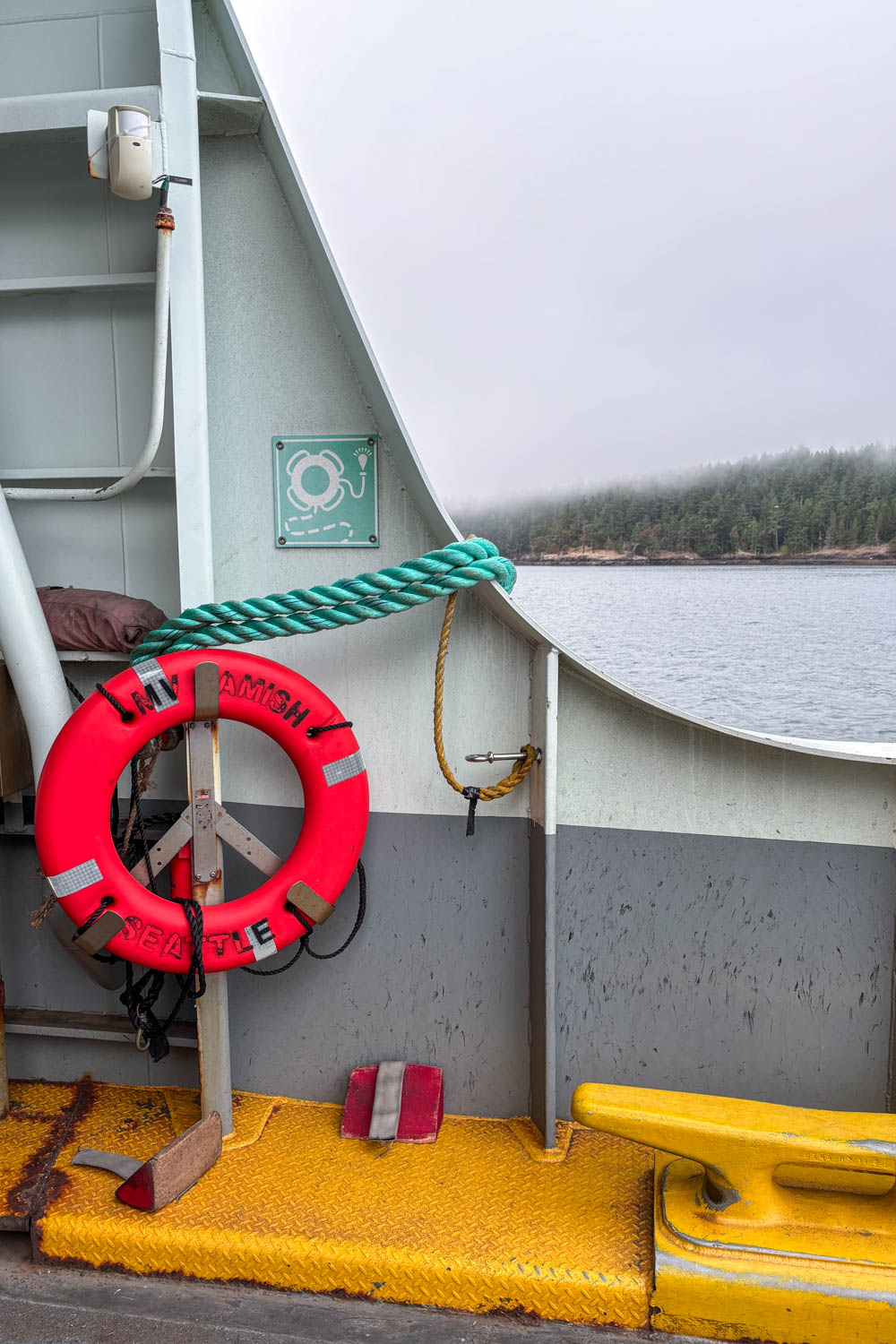 Looking out from ferry with a neon orange life preserver in the foreground and a fog-shrouded island in the background