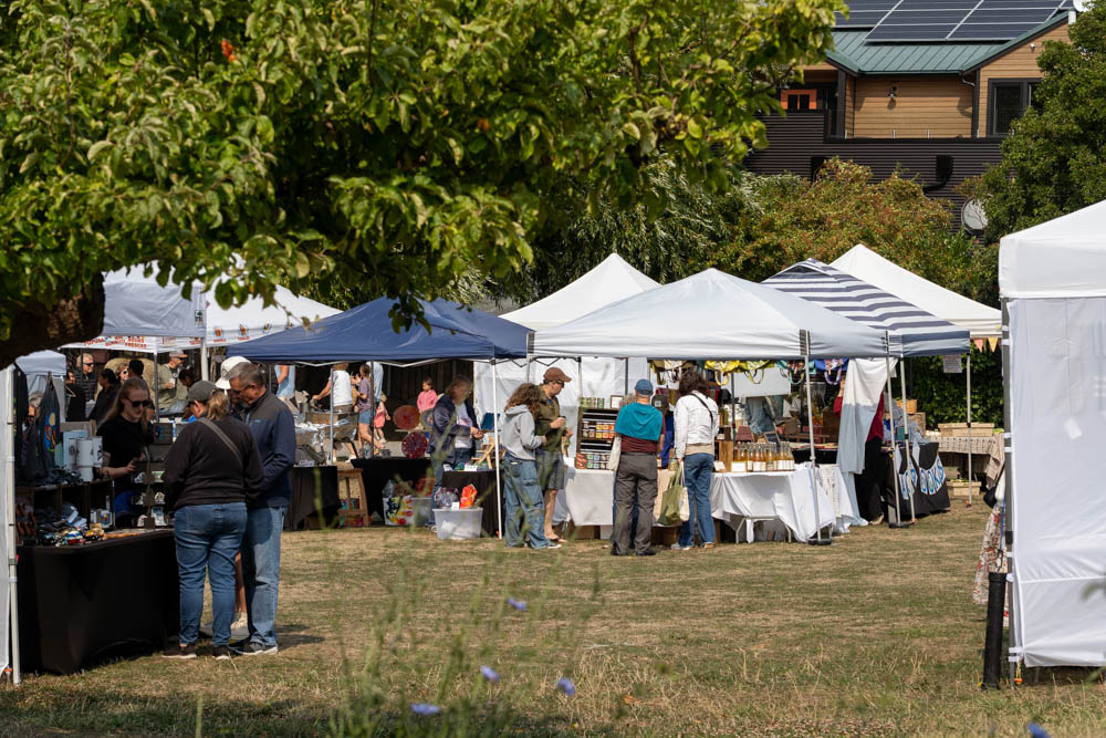 Shoppers at various tents viewed beneath leafy tree