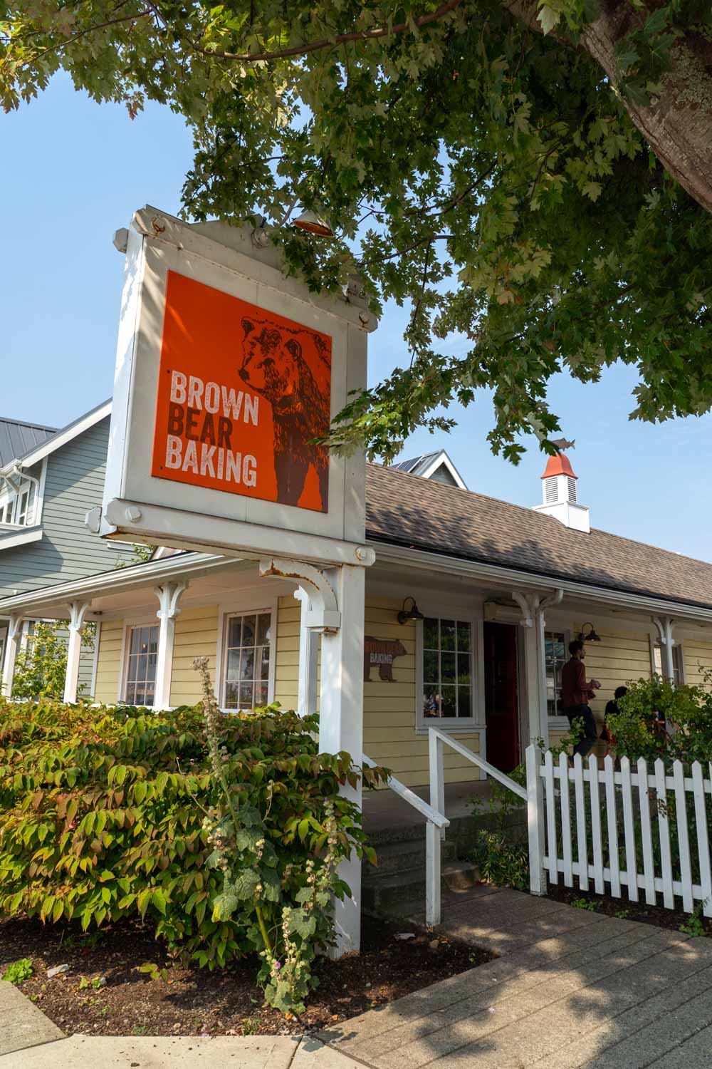 Brown Bear Bakery building and sign, framed by leafy tree and hedge