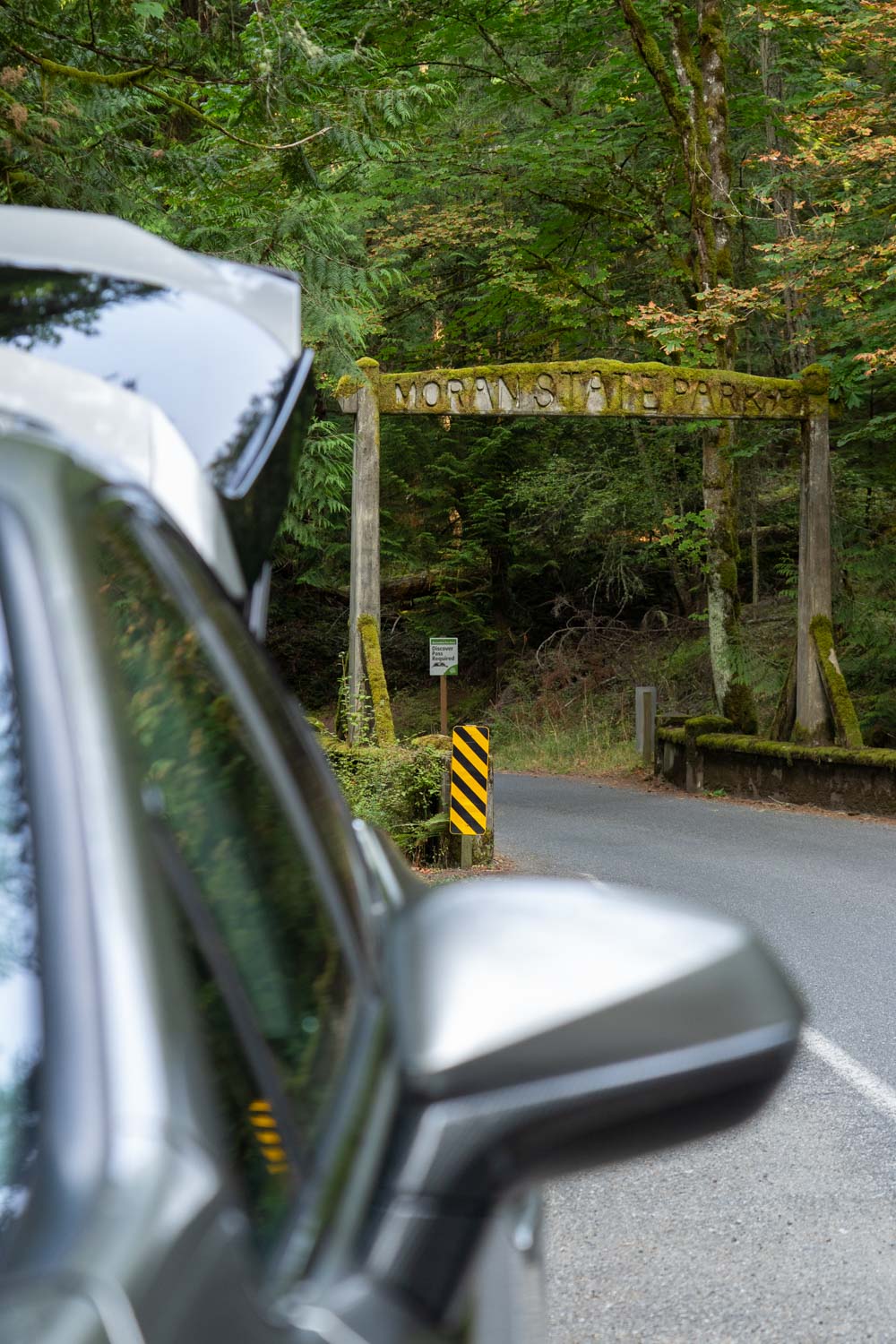 Moss-covered, historic archway to Moran State Park with silver vehicle in the foregound