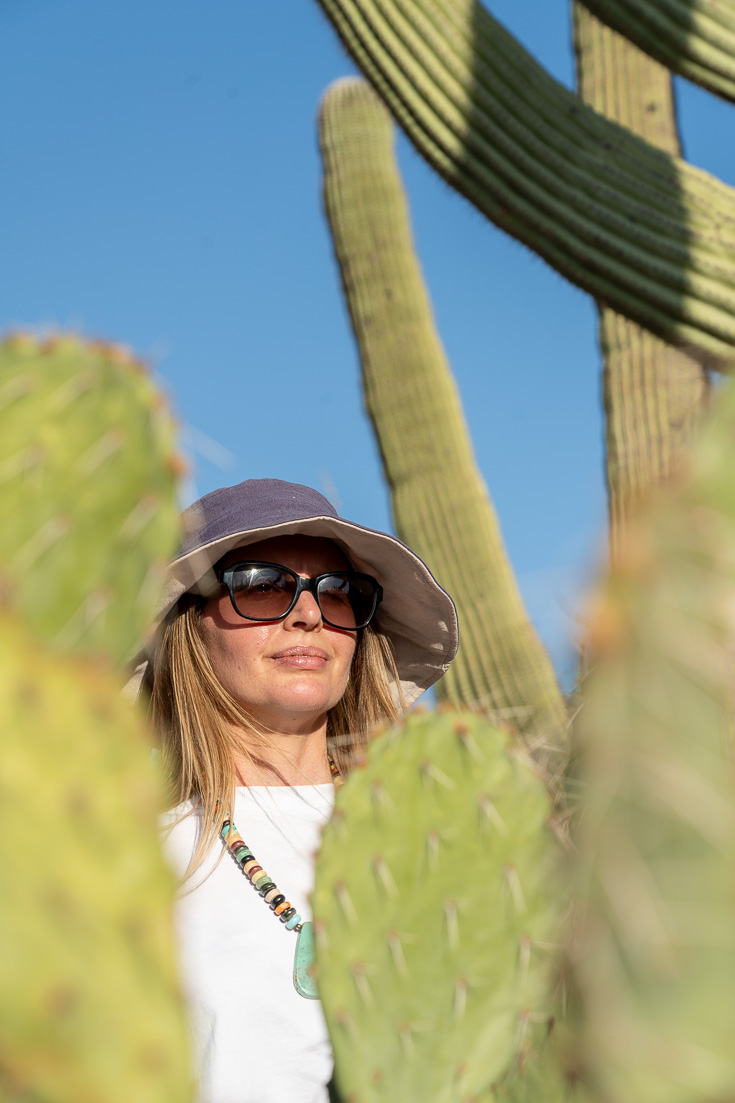 Madam ZoZo in sunglasses and hat, viewed through cacti foliage 