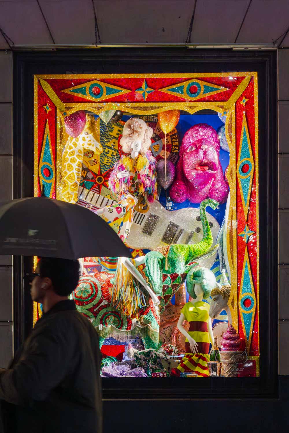 Bergdof Goodman department store holiday window, illuminated at night with the silhouette of a passing man holding an umbrellas