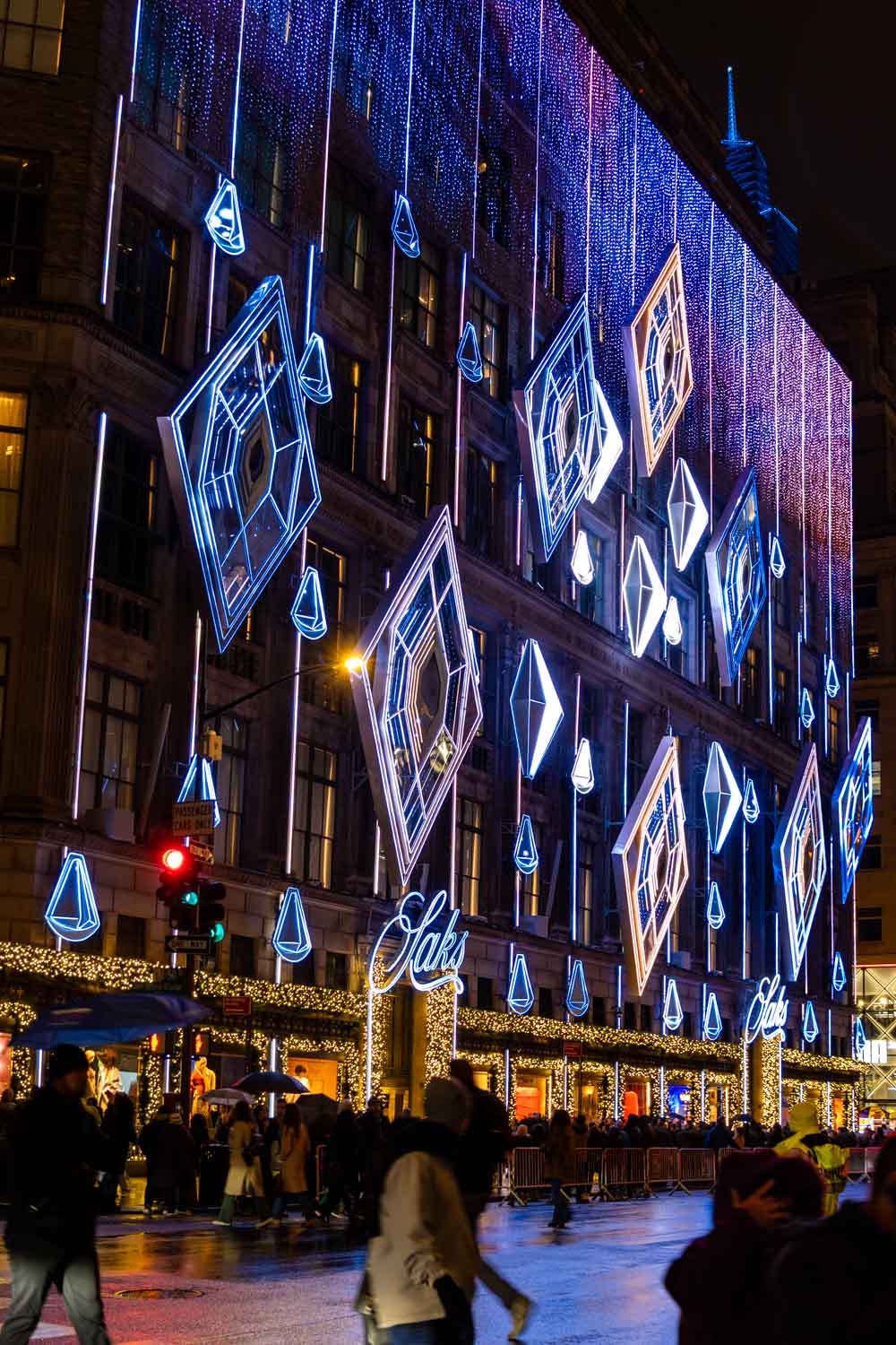 Saks Fifth Ave lighting show with various-size illuminated diamonds on storefront, reflected on wet street