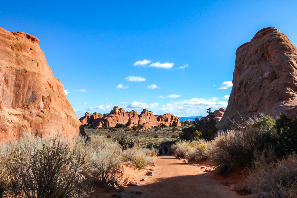 View of hiking trail passing between two rock formations with rock spires in the distance ahead