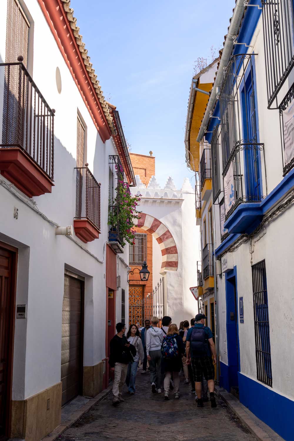 Tourist group filing down narrow Cordoba street with city gate at the end