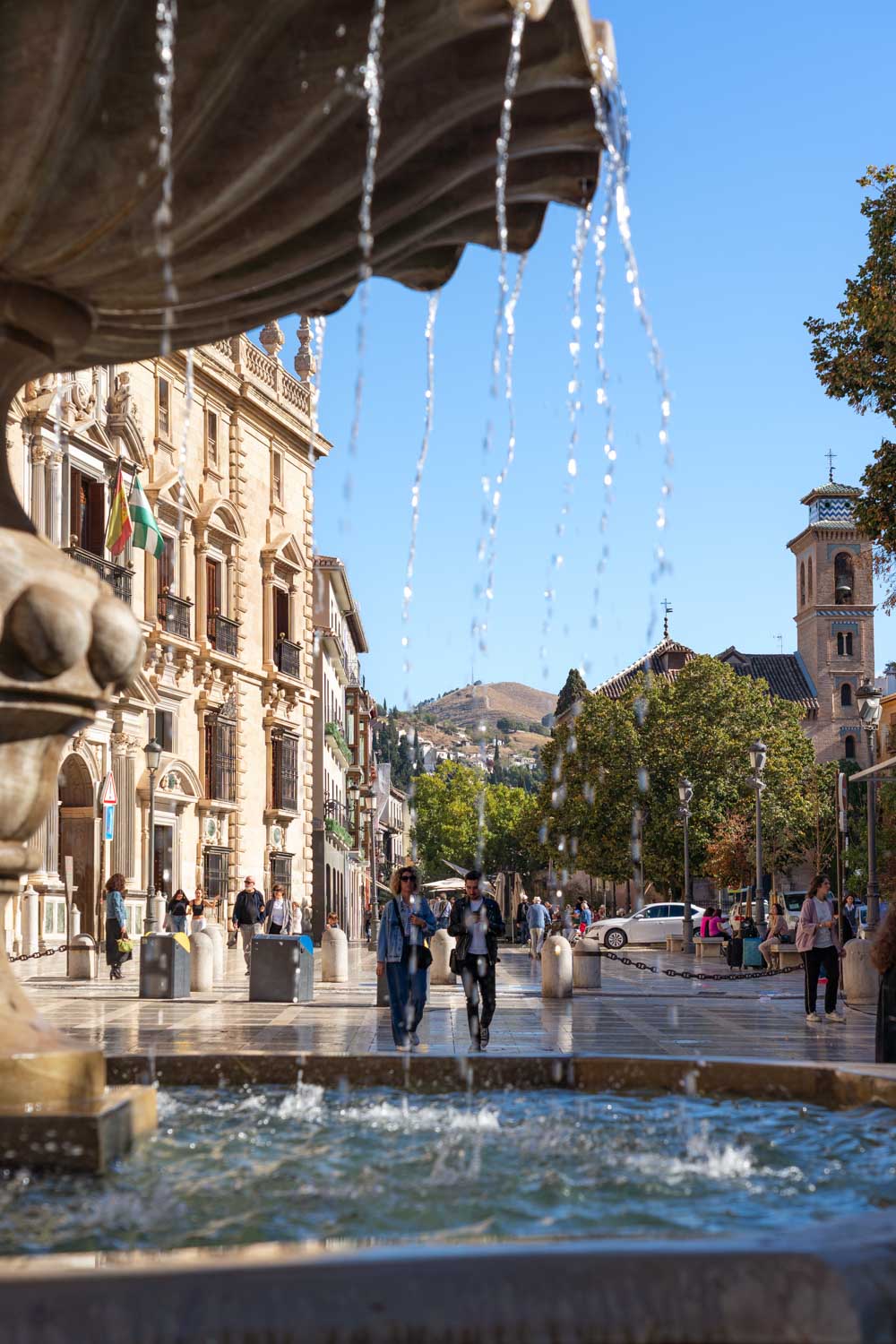 Plaza in historic district viewed through water from a fountain, with mountains in distance