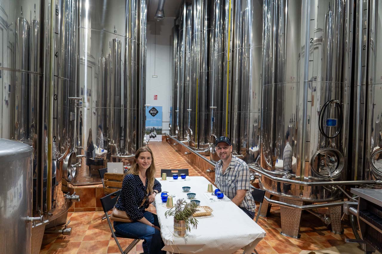 Couple sitting at tasting table in a room with silver vats of olive oil