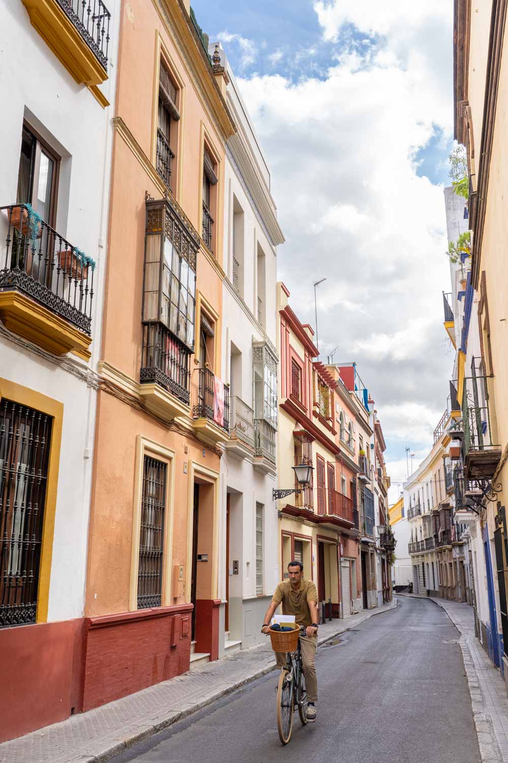 Man riding bicycle down quiet, narrow street lined with colourful homes