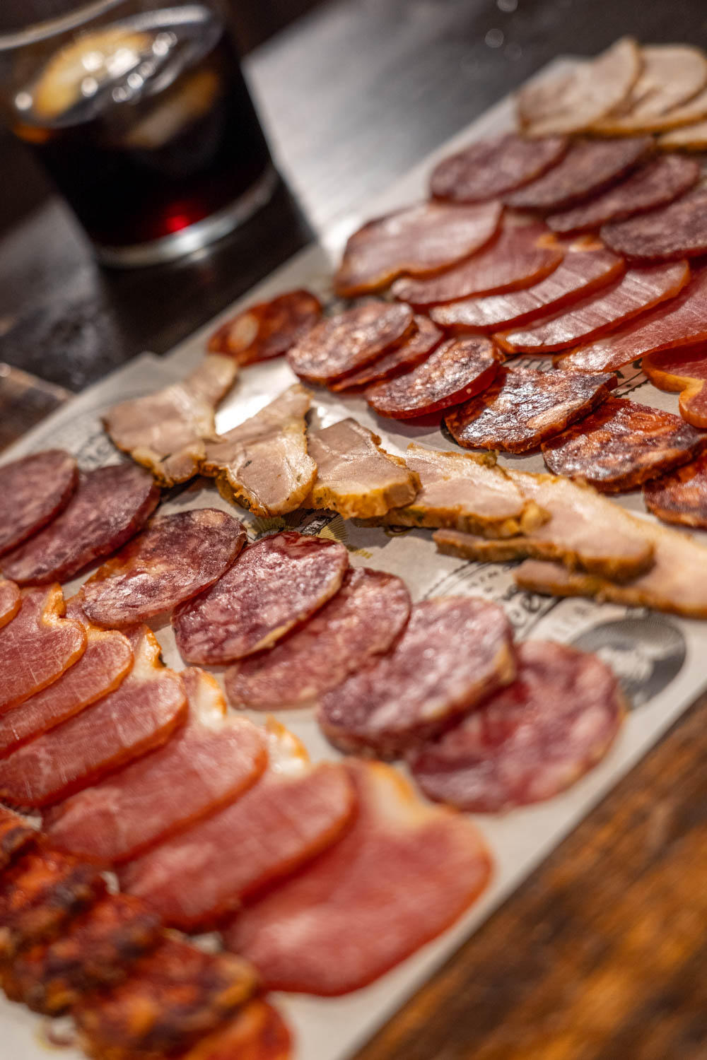 A platter of charcuterie for tasting with a glass of vermouth in the background