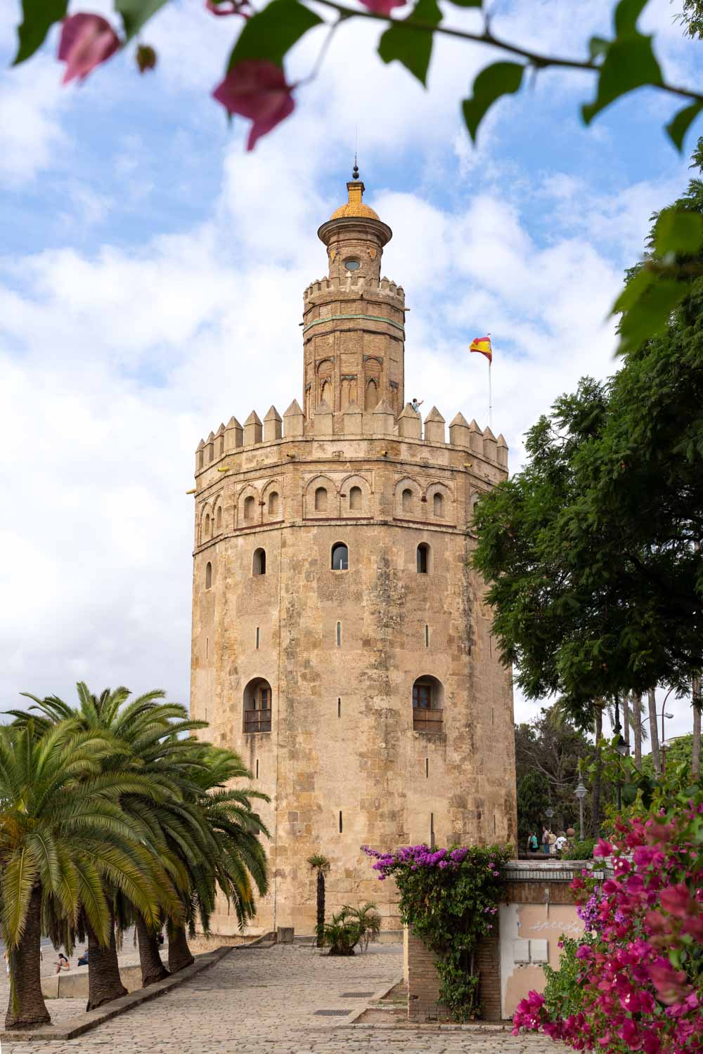 A dodecagonal watchtower framed by palms, bouginvilleas and other vegetation