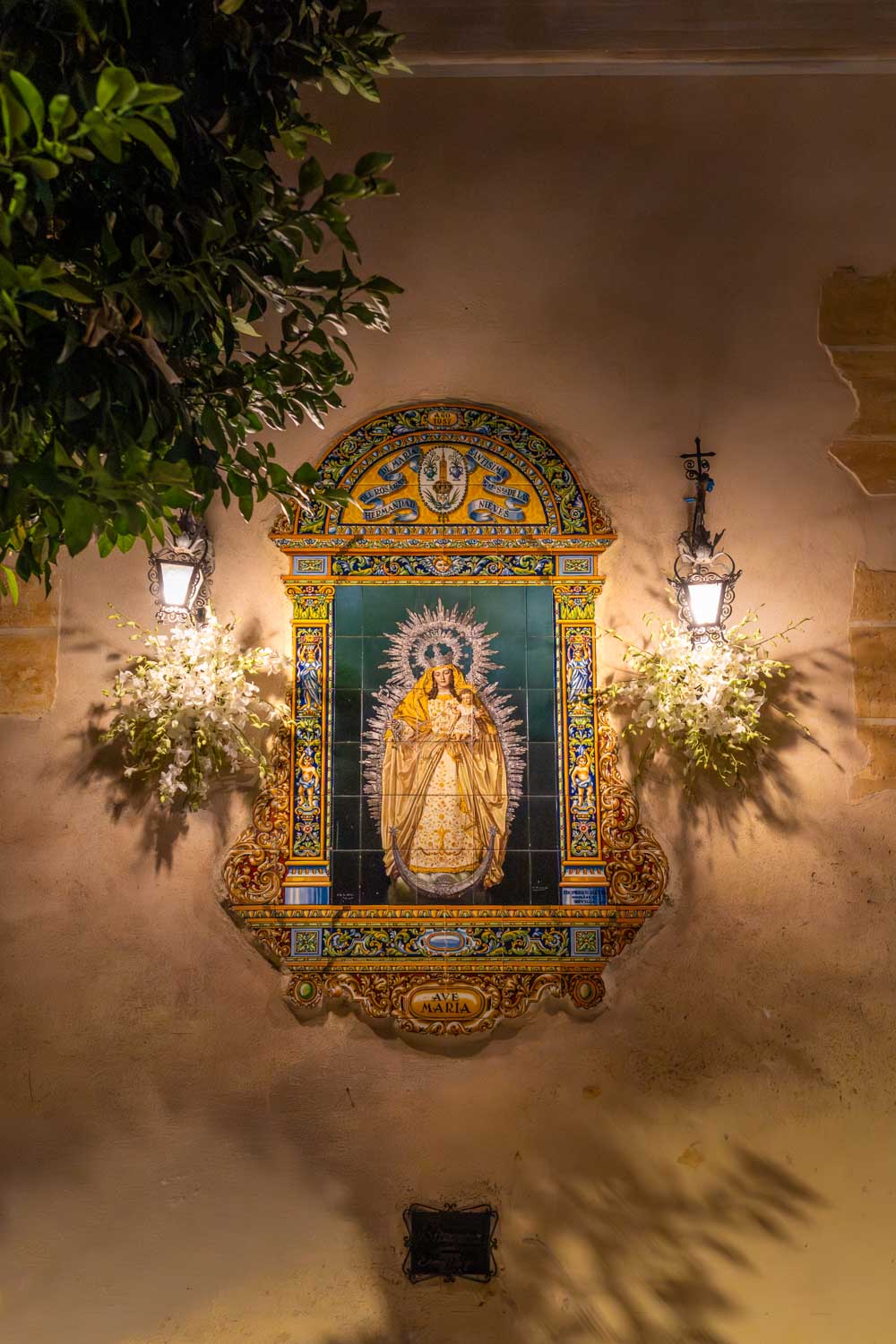 Tiled shrine to Virgin Mary lit up in a Seville street at night