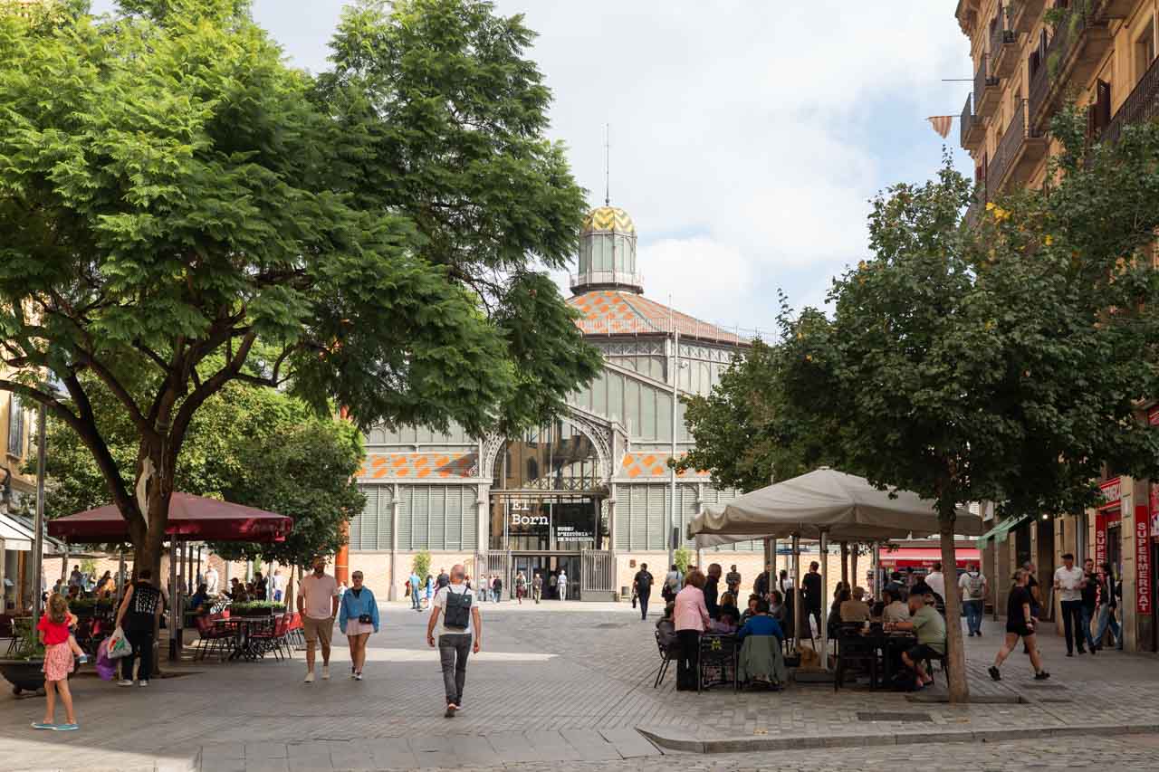 Market building viewed down short street lined with trees and diners under umbrellas