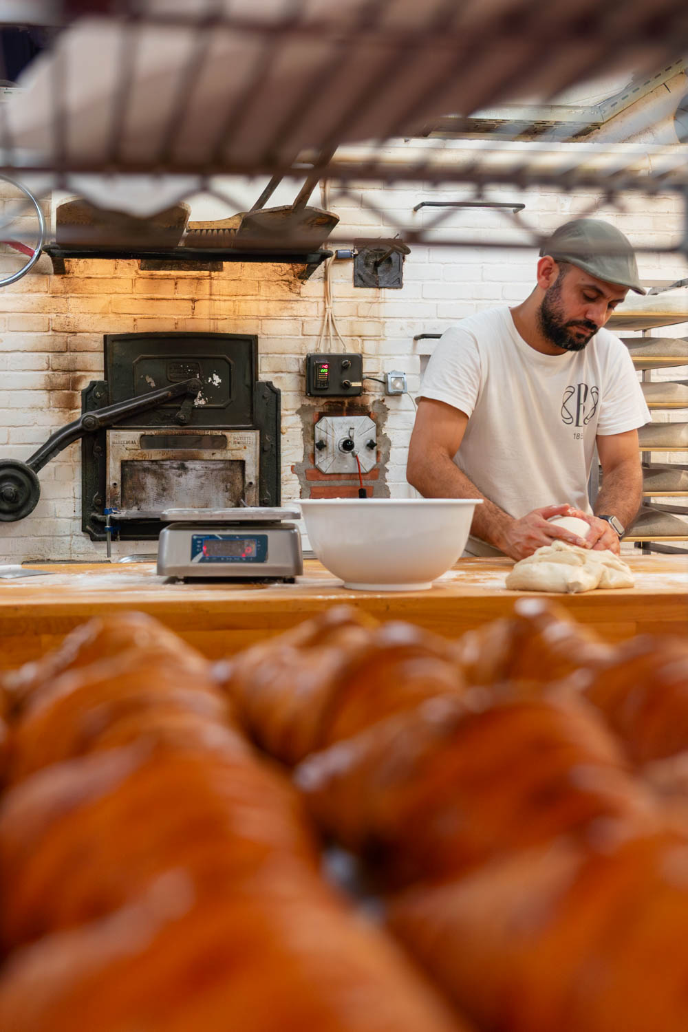 Baker kneeding dough besides historic oven with crossiants in foreground