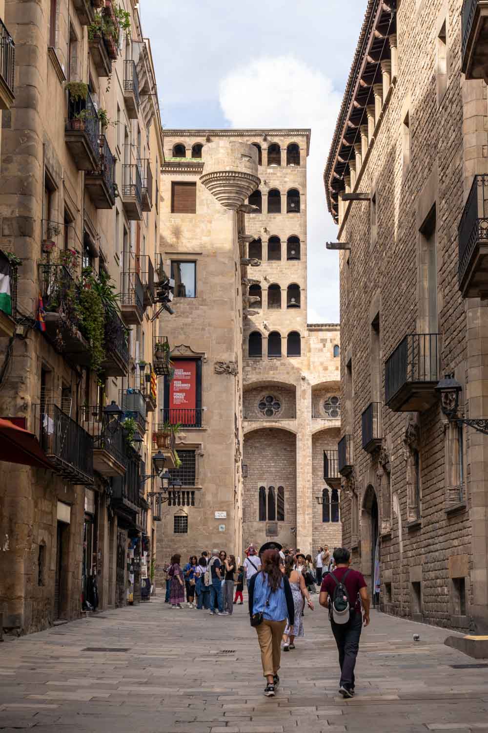 Pedestrians walking down street toward 14th-century medieval public square and palace facade with many arches 