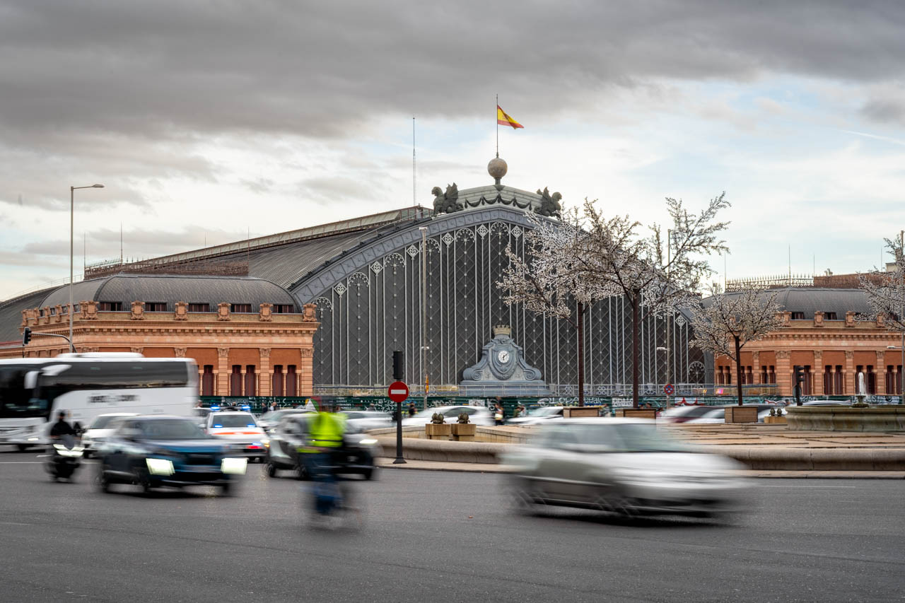 Large cast iron and glass train station viewed across street with passing traffic