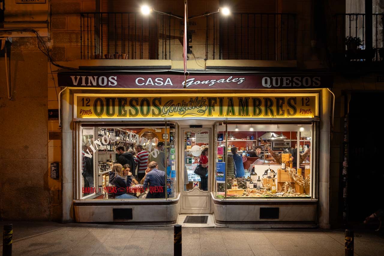 Storefront of tapas bar Casa Gonzalez at night, with diners and cheese display in the front window
