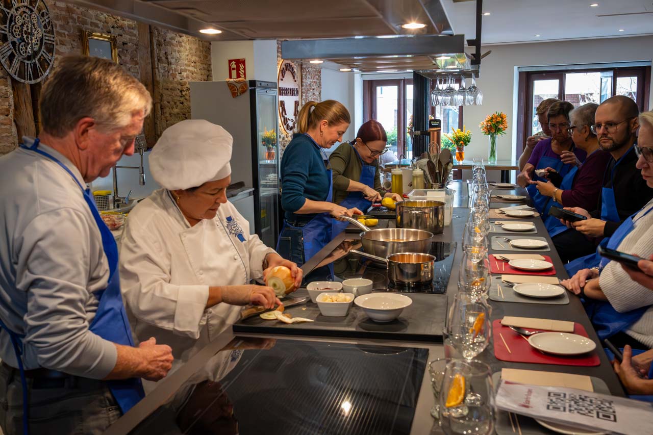 International tourists in blue aprons, learning to make Spanish dishes in kitchen with chef