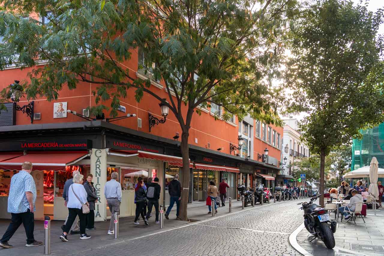 Red exterior of market viewed from tree-lined street, with pedestrians passing by