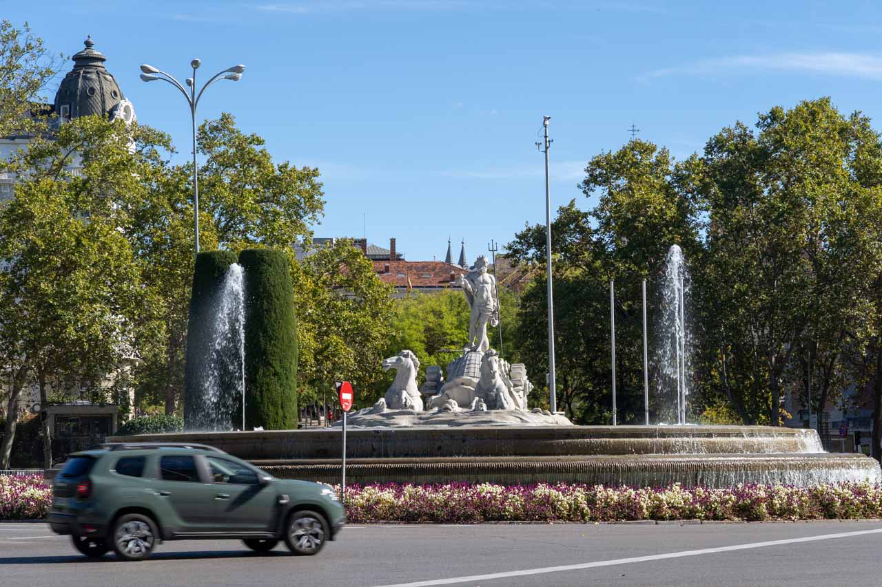 Large flower rimmed fountain of Neptune on a sunny day, with passing car