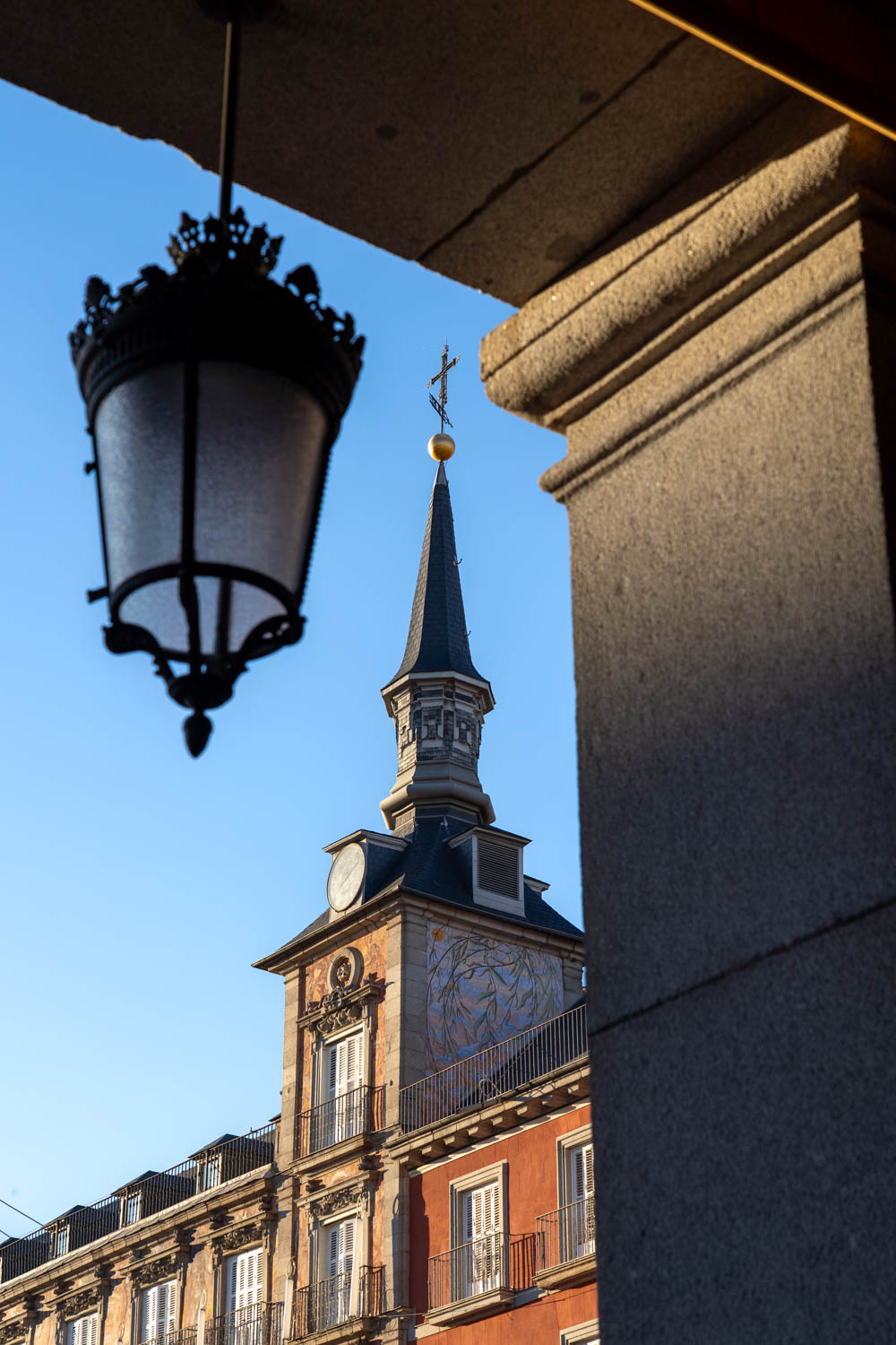 Spire on Plaza Mayor architecture, framed by gate and lantern-style lighting