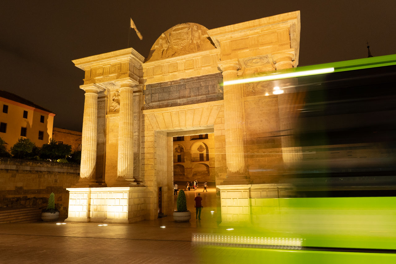 Green bus passing Puerta del Puente at night