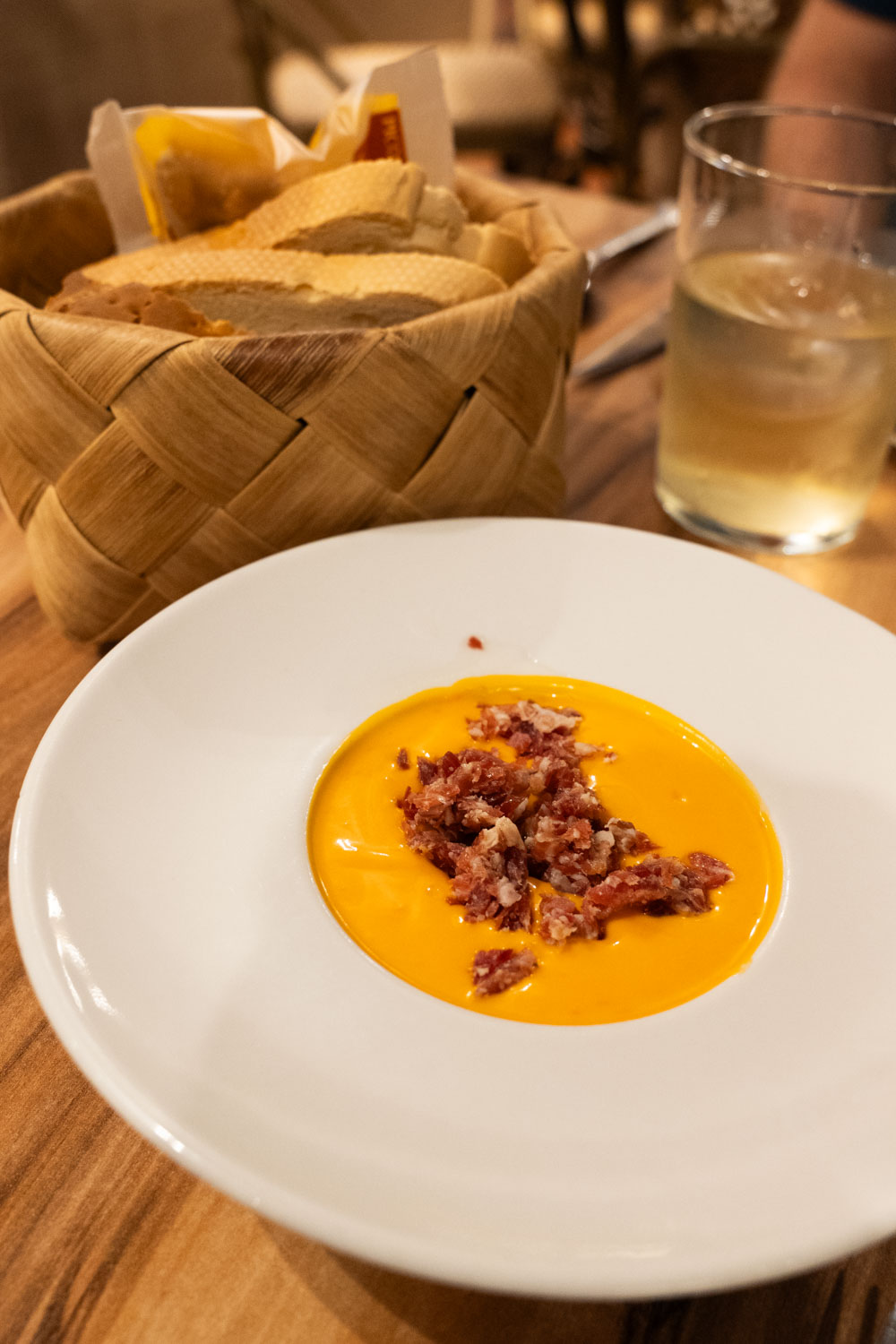 Salmorejo presented in white dish with basket of sliced bread in the background