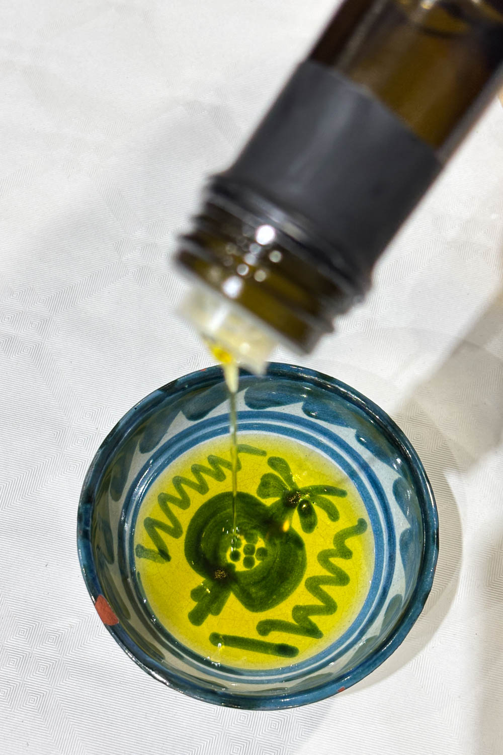 Olive oil being poured into a blue and white ceramic dish with a pomegranate painted on the bottom