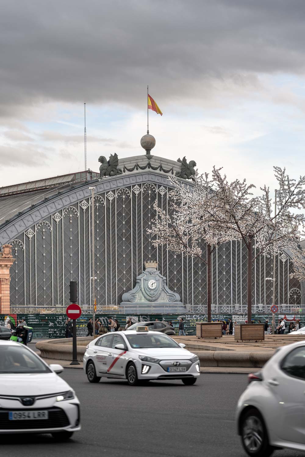 Large cast iron and glass train station viewed across street with passing taxis